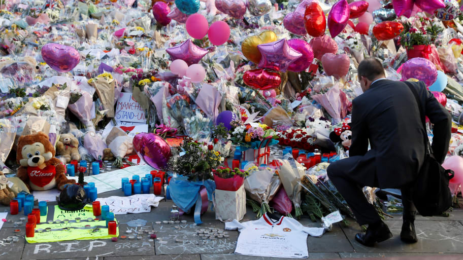 A man crouches in front of flowers, messages, and tokens left in tribute to the victims of the attact on Manchester Arena, in central Manchester, Britain, May 26, 2017.
