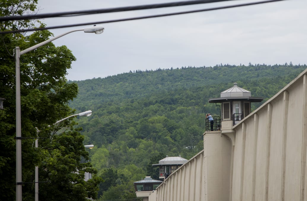A guard peers out from a tower at an upstate New York prison, with mountains looming in the background.