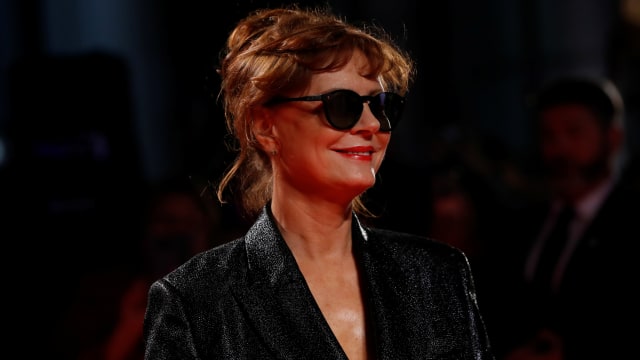 Susan Sarandon, wearing a black dress and glasses, smiles at a film festival.