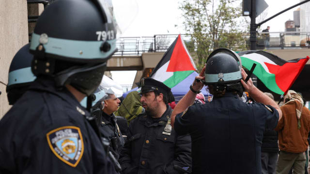 NYPD officers stand in front of protesters waving Palestinian flags.