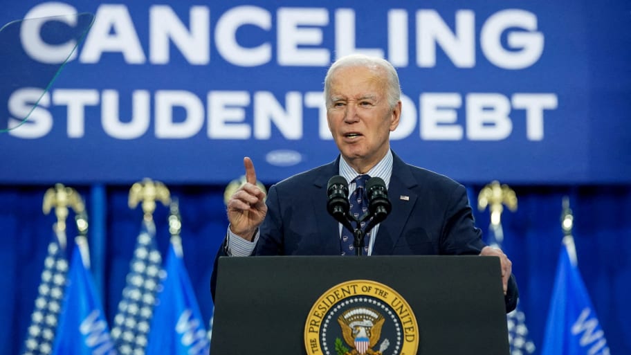 Joe Biden speaks on stage with a screen saying “canceling student debt” in background