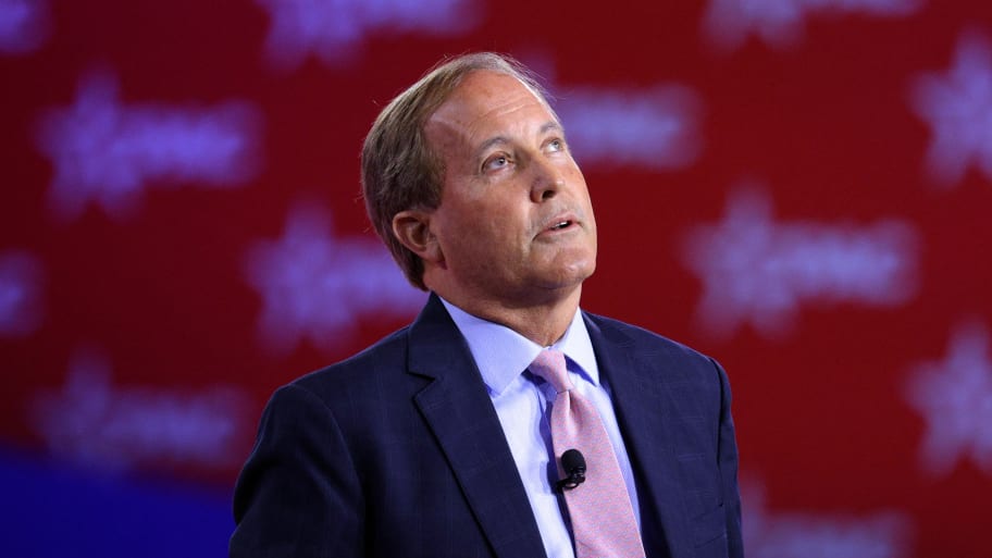 Ken Paxton, wearing a suit and tie, stares up as he’s on stage at a CPAC event.