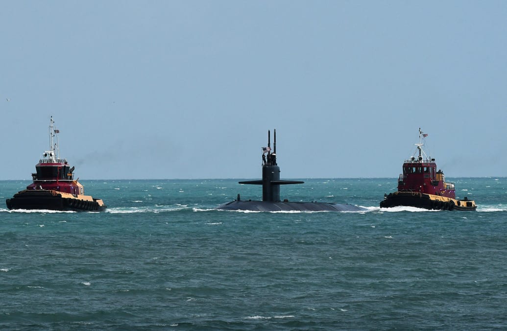 A photo of tugboats guiding a nuclear-powered U.S. Navy submarine into port.