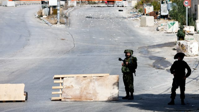 A photograph of Israeli soldiers standing guard on a blocked road, as the entrance to Hebron is closed, in the Israeli-occupied West Bank, October 8, 2023.