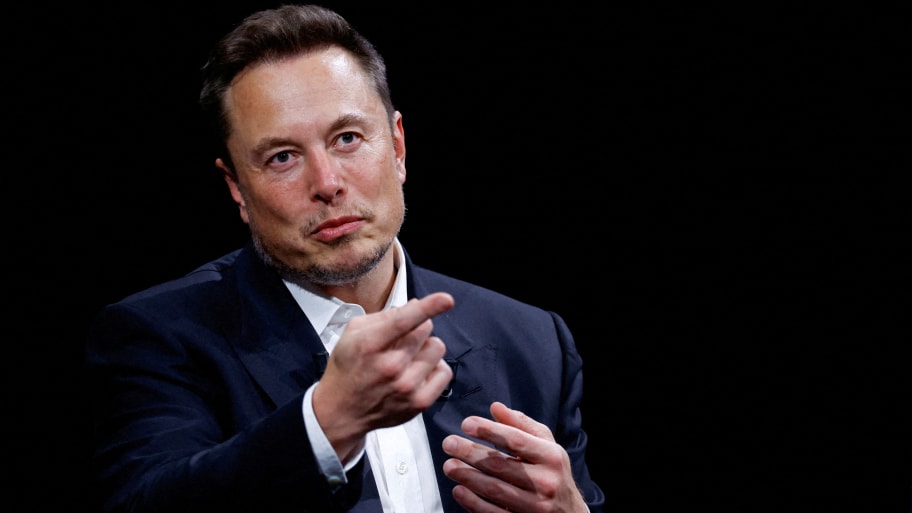 Elon Musk points forward while on stage at an event.