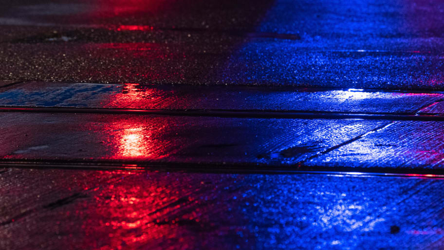 Police blue lights and a red traffic light reflect on a wet road with a streetcar track