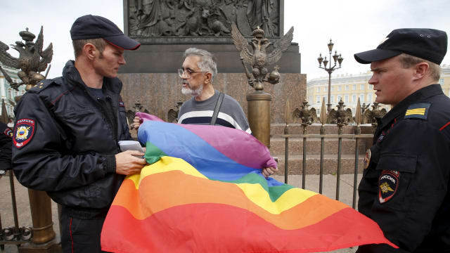 Policemen talk to a gay rights activist holding a rainbow flag during a protest in Dvortsovaya Square in St. Petersburg, Russia, Aug. 2, 2015. 