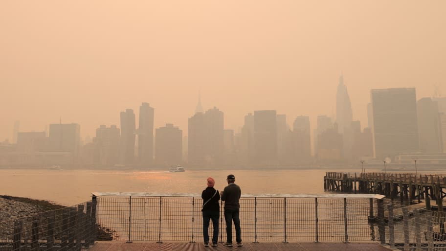 "People watch the sunset as haze and smoke caused by wildfires in Canada hang over the Manhattan skyline.