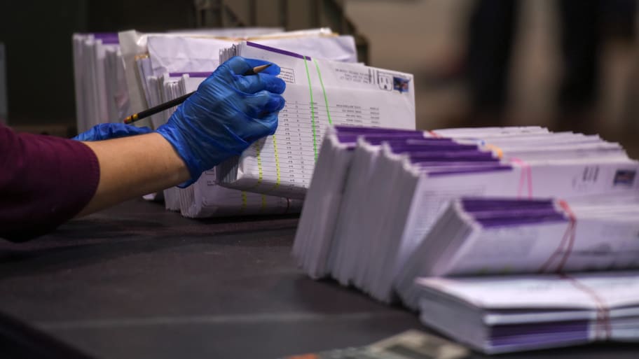 A photo of an election worker’s latex-gloved hand, processing mail-in ballots.