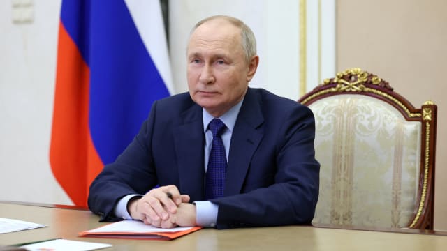 Russian President Vladimir Putin sits in char before Russian flag
