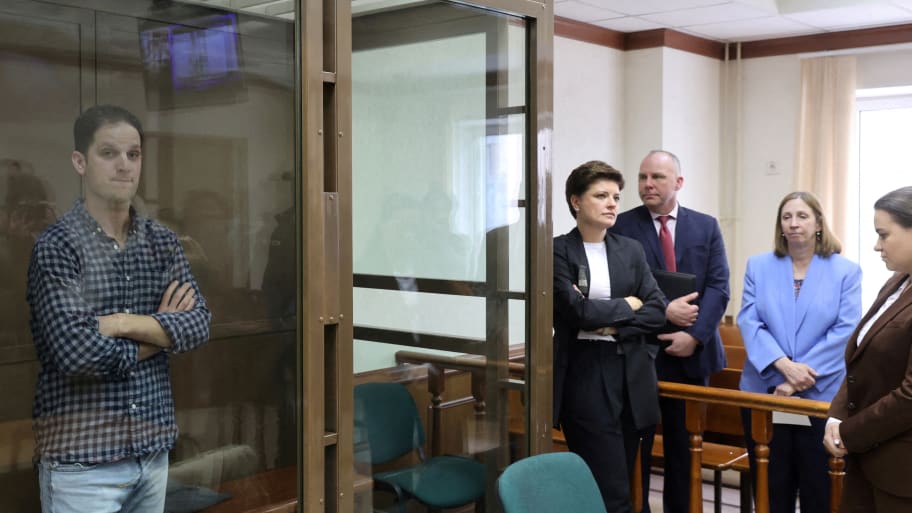 Wall Street Journal reporter Evan Gershkovich stands behind a glass wall of an enclosure for defendants.