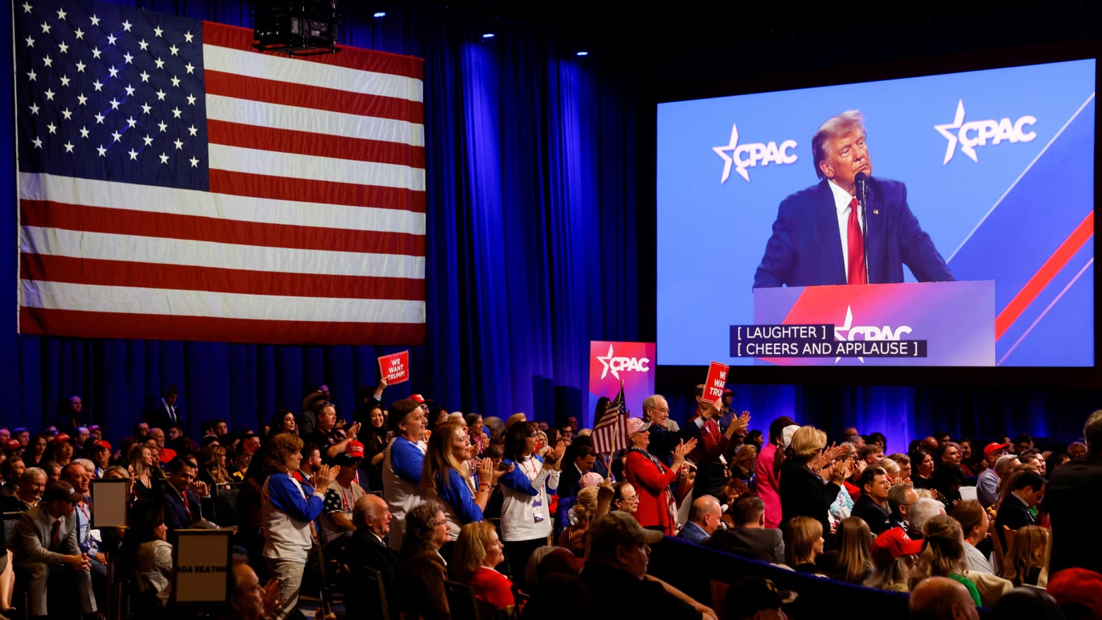 A monitor shows Donald Trump speaking at CPAC as supporters in the crowd cheer
