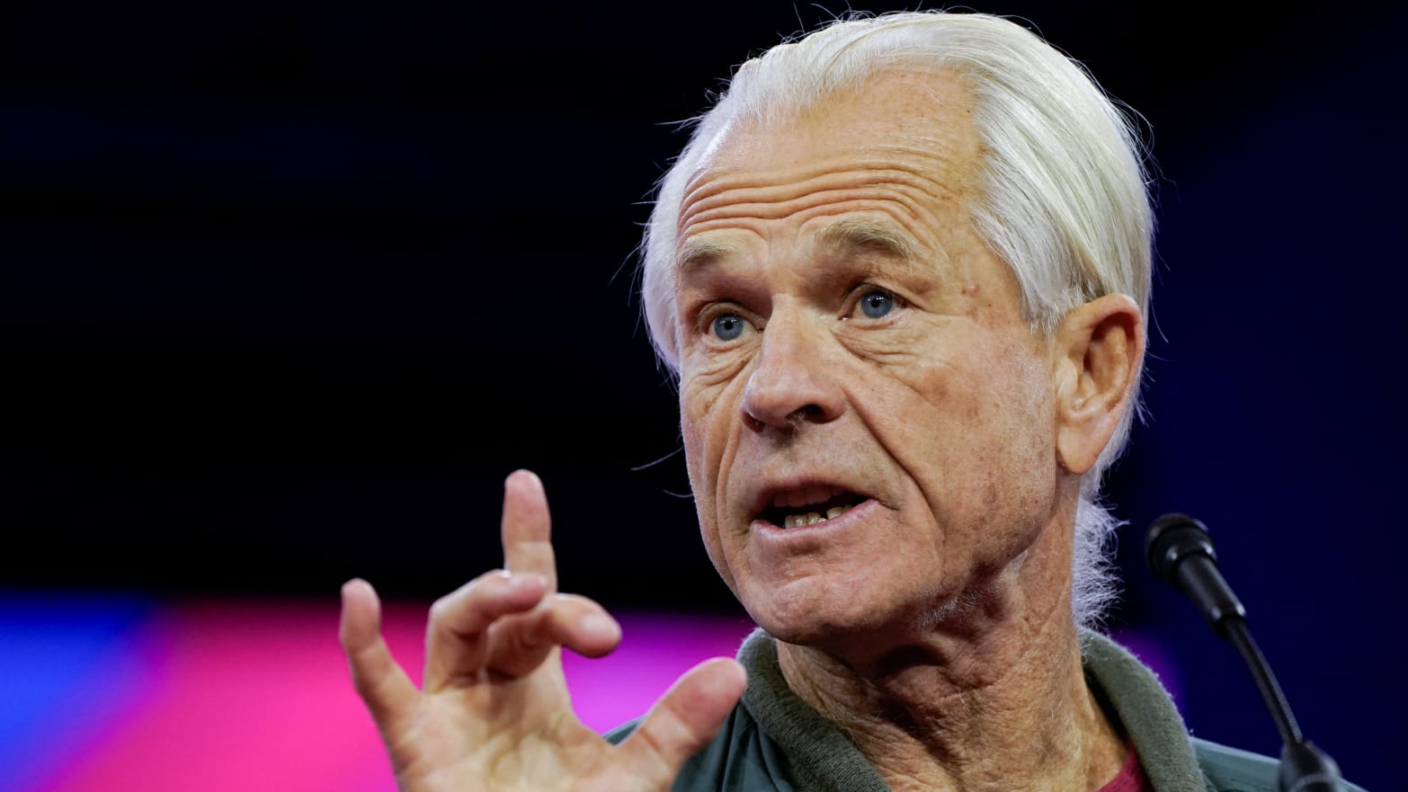 Peter Navarro speaks and raises his right hand on stage at CPAC.