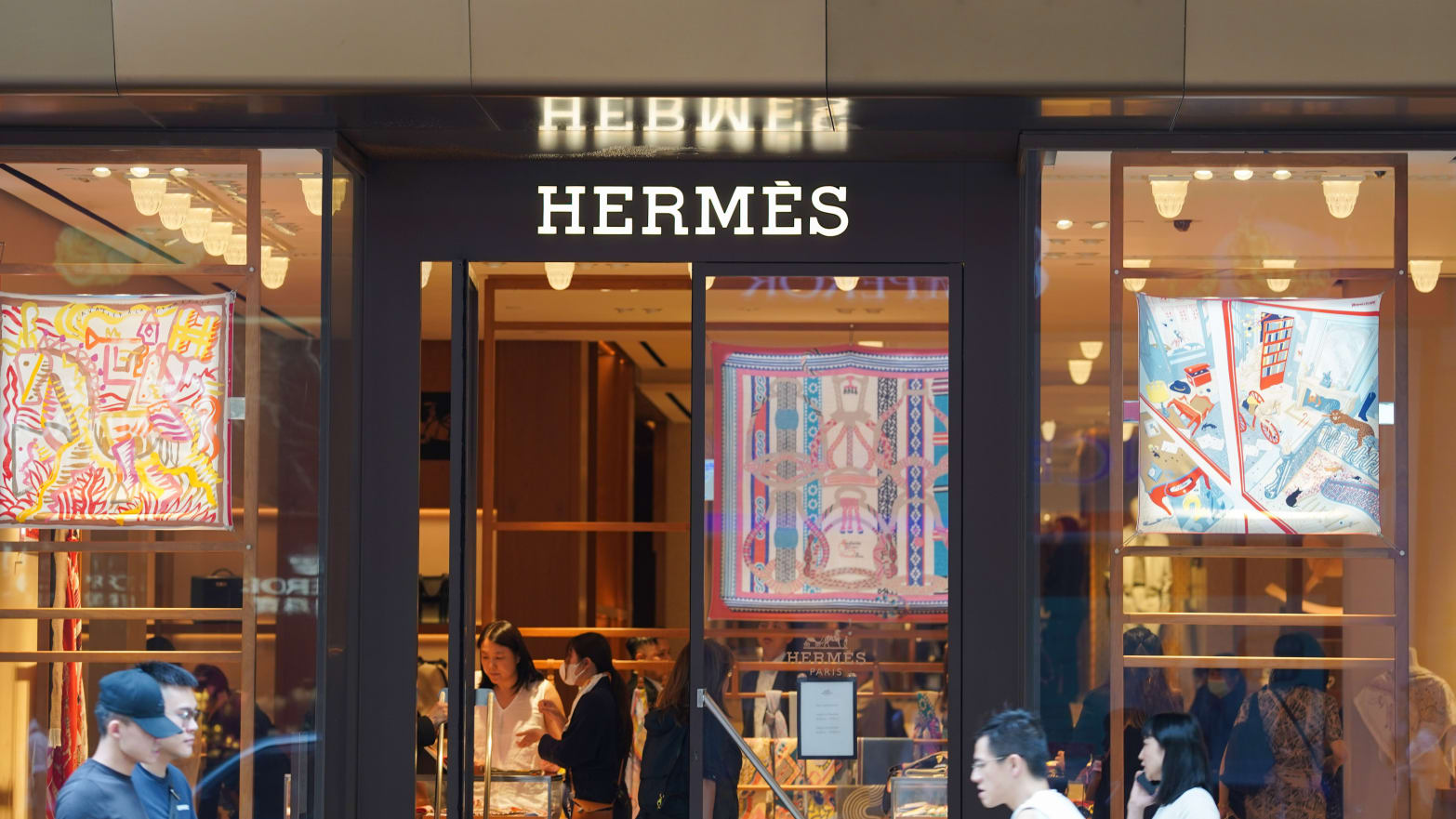 Pedestrians walk past the French luxury design house Hermès logo and store at Harbour City in Hong Kong. 