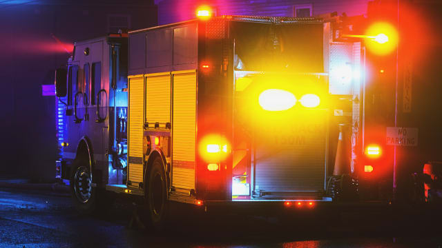 A firetruck's bright lights are reflected on the surface of a wet street.