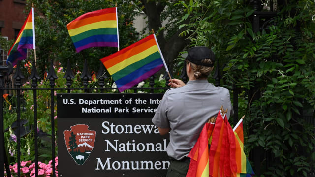 A National Park Service ranger places rainbow flags on the fence at the Stonewall National Monument