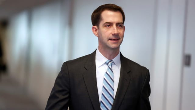 Tom Cotton smirks as he walks in the Senate, wearing a suit and tie.