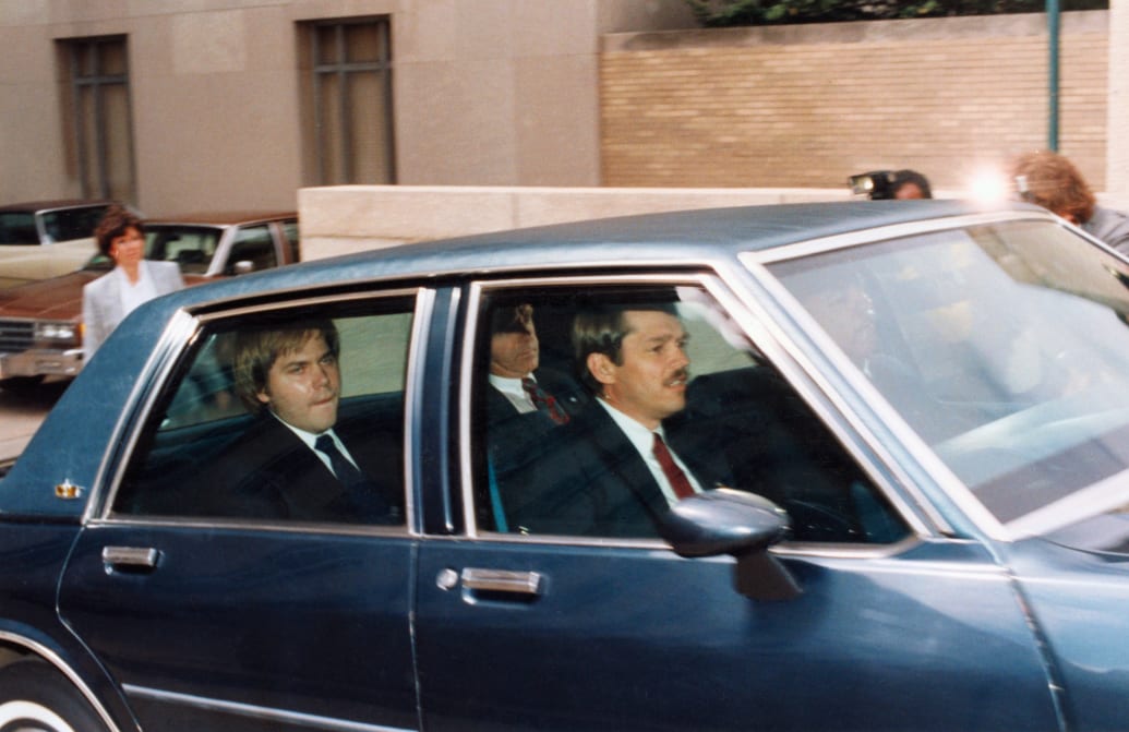John Hinckley, Jr., charged with attempting to assassinate President Reagan, sits in the back of an official vehicle in DC federal court.