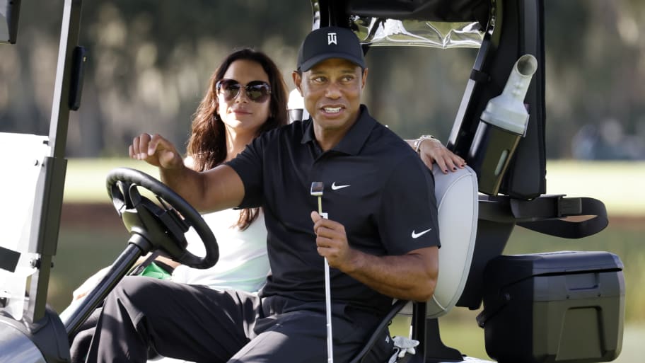 Erica Herman and Tiger Woods ride in a golf cart, with im driving