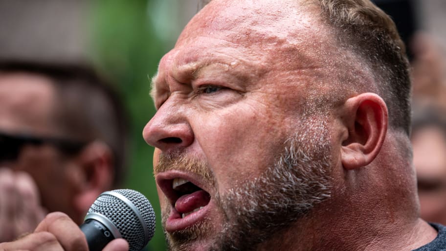 Alex Jones yelling into a microphone at a protest outdoors.