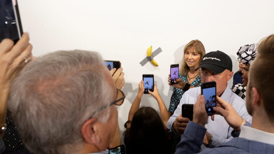 A woman poses for a photo next to a banana attached with duct-tape that replaces the artwork “Comedian” by the artist Maurizio Cattelan,