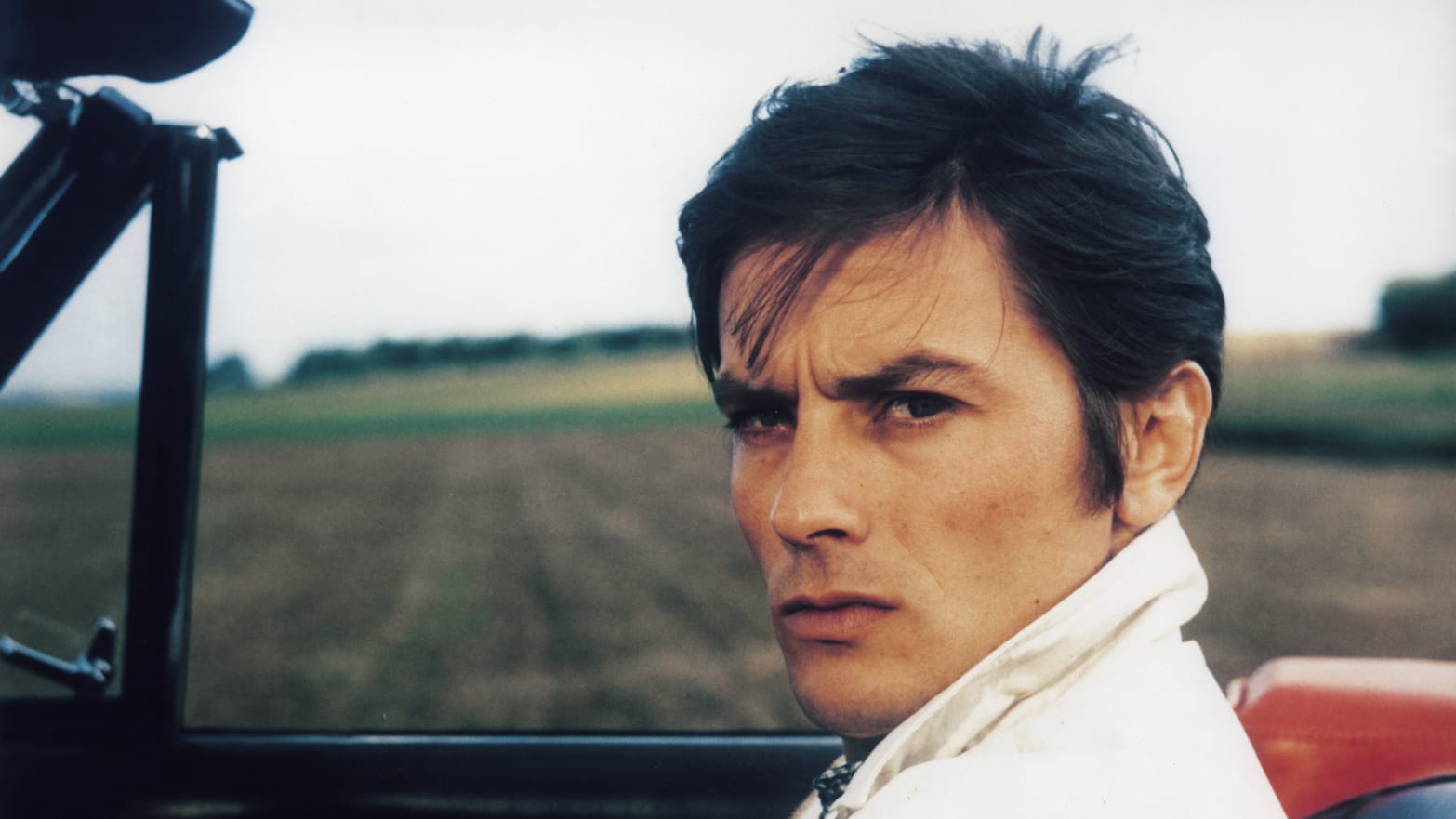 French actor Alain Delon smirks in a car on the set of "Diaboliquement Vôtre," directed by Julien Duvivier.