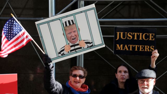 A protester holding a sign with a photo of Trump behind bars.