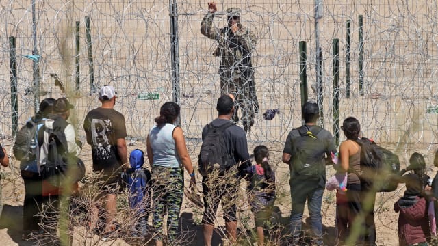 Migrants seeking asylum in the U.S. speak with a Texas National Guard agent through a barbed-wire fence.