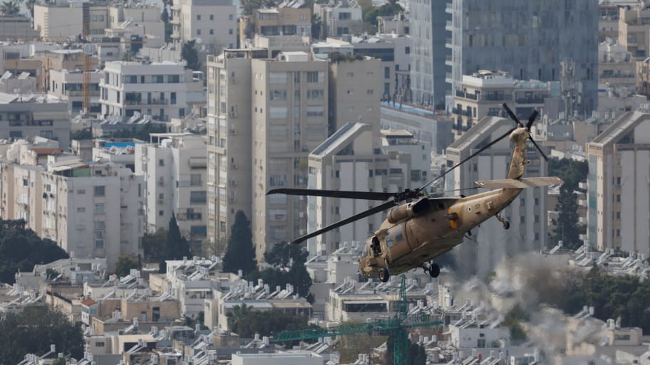 An Israeli helicopter flies over Israel, with apartment buildings in the background.