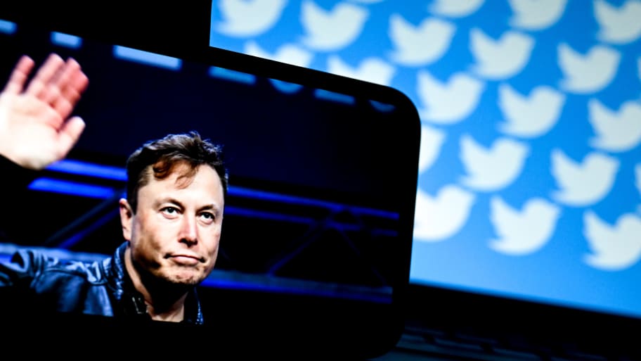 Elon Musk's photo is displayed on a phone screen with logo of 'Twitter' in the background on a computer screen