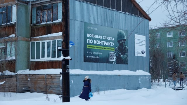 A photo of a woman walking past a military banner in Russia.