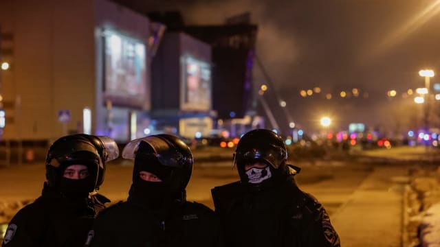Law enforcement officers in masks stand guard near the burning Crocus City Hall venue