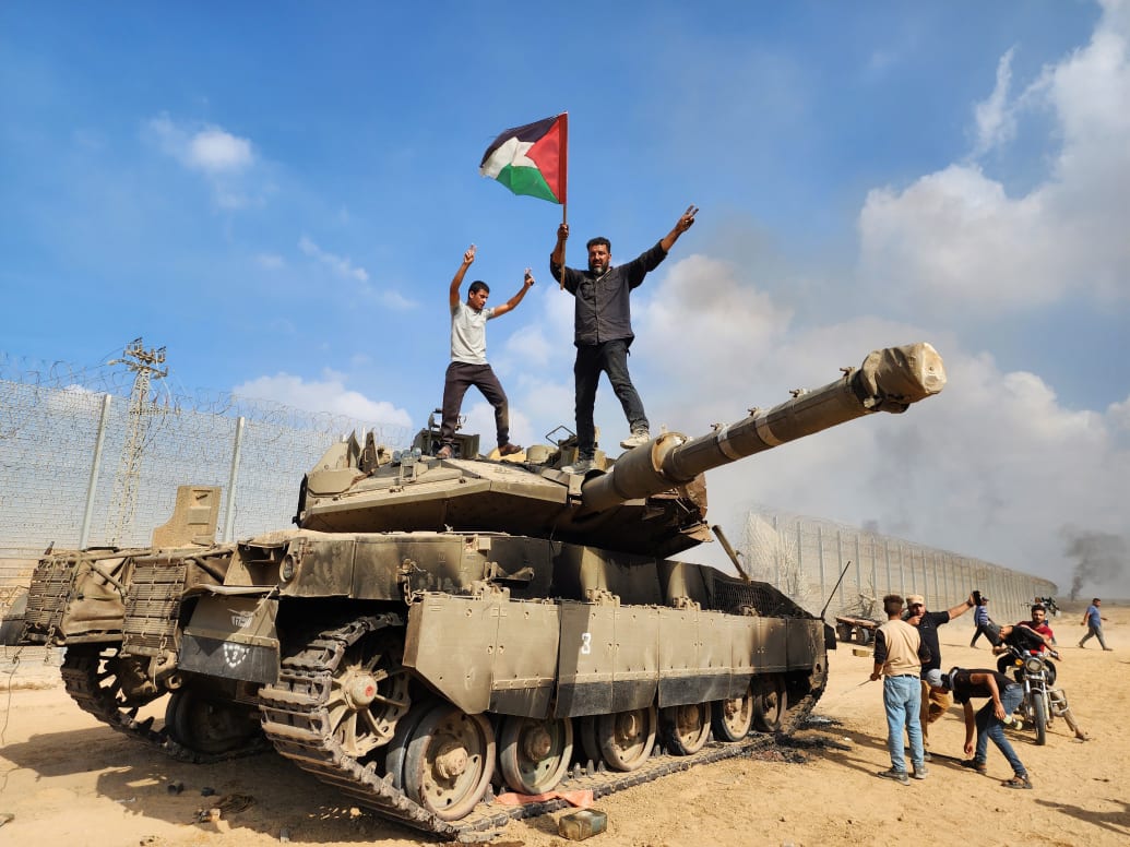Photo of Hamas supporter holding a Palestinian flag atop of destroyed Israeli tank