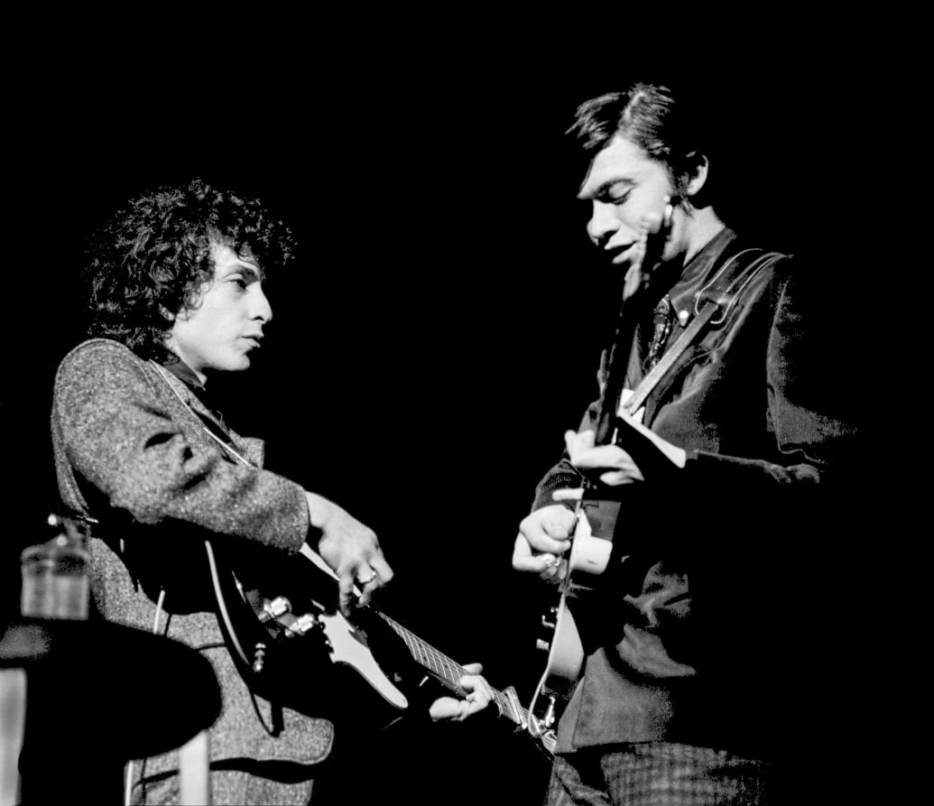 An image of  Bob Dylan (L) and Robbie Robertson (R) playing electric guitars during Dylan's 2nd set at the Academy of Music on February 24, 1966.