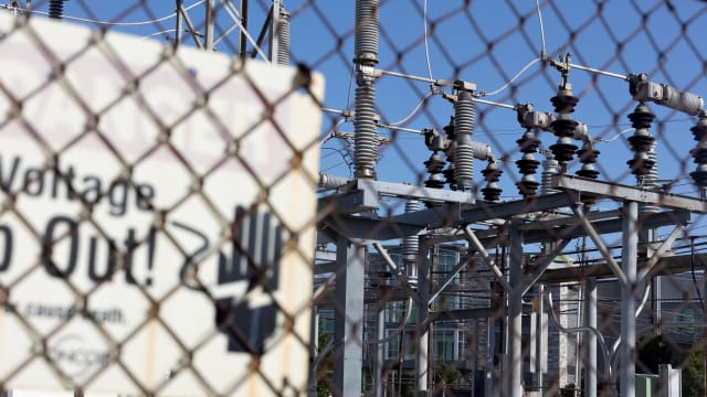 A photo of power lines at an electrical substation, with a fence and a sign warning trespassers to keep out.