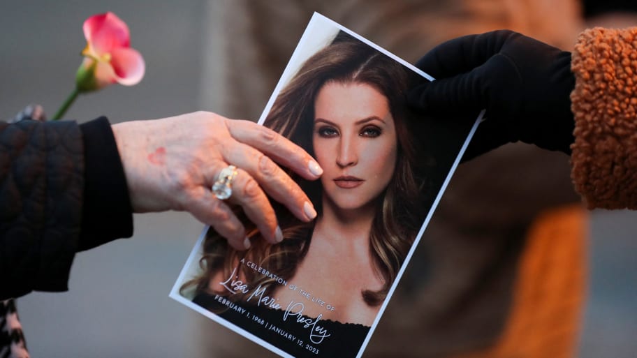 A music fan hands a picture of Lisa Marie Presley to another fan as they attend a public memorial for her. Her cause of death was recently revealed to be complications from a small bowel obstruction.