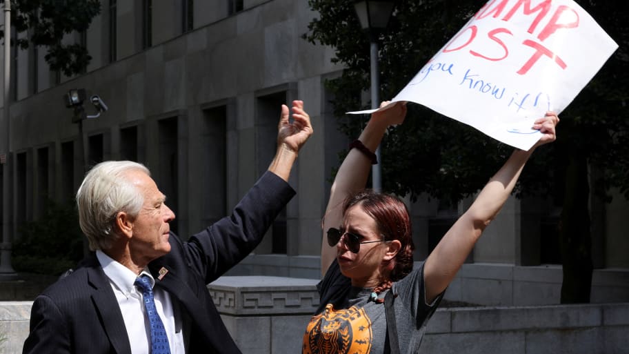 Peter Navarro, a White House economic adviser under former U.S. President Donald Trump, tries to grab a protestors sign while speaking to reporters