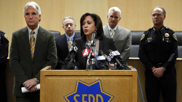 Kamala Harris in front of a S.F.P.D branded lectern with a police officer behind her