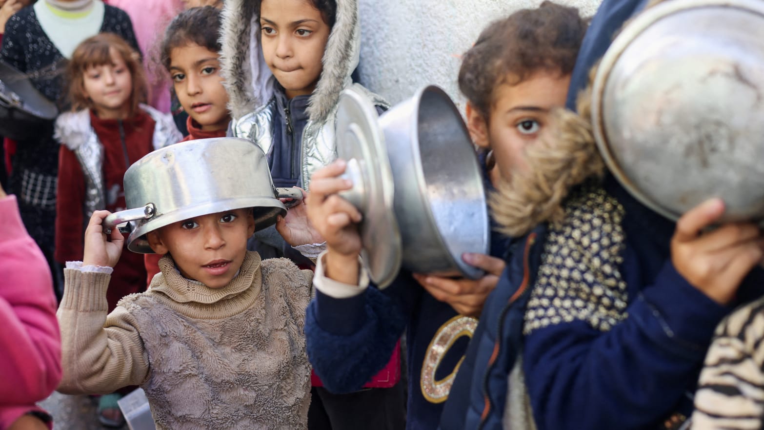 Palestinian children carry pots as they line up to receive food cooked by a charity kitchen in Rafah in southern Gaza.