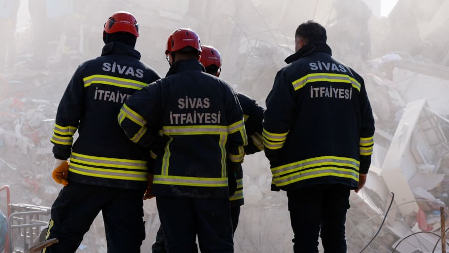 Fire fighters look at the debris surrounded by smoke coming from the extractors, following the deadly earthquake in Maras, Turkey, February 11, 2023. 