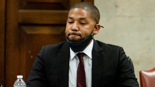 Jussie Smollett, wearing a suit with a face mask pulled down on his chin, listens in a courtroom.