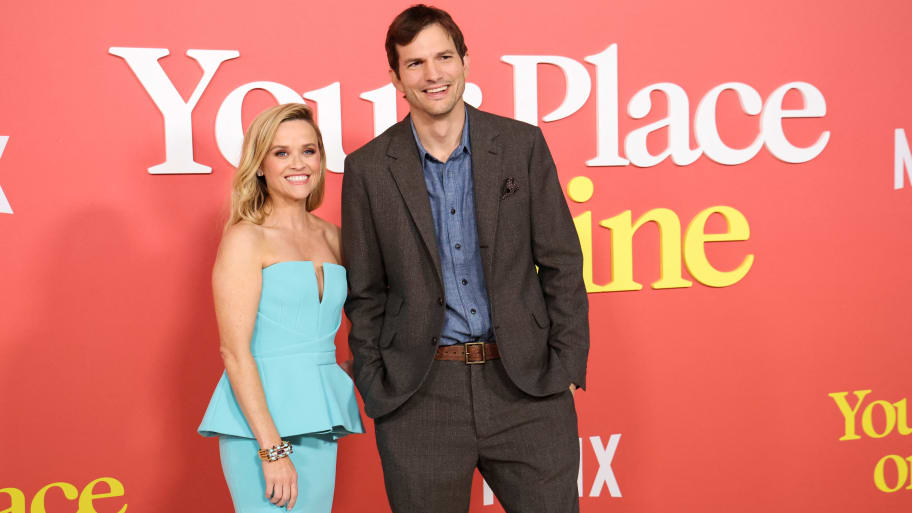Reese Witherspoon and Ashton Kutcher smile next to each other, as he puts his hands in his pockets.