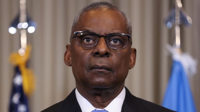 Lloyd Austin, wearing glasses and a suit, stares forward blankly.
