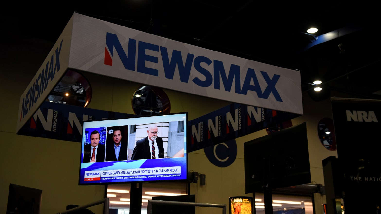 A Newsmax booth broadcasts as attendees try out the guns on display at the National Rifle Association (NRA) annual convention 