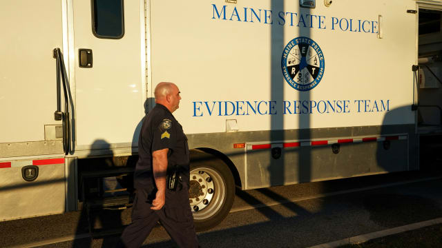 A cop walks in front of a Maine State Police evidence response team vehicle.