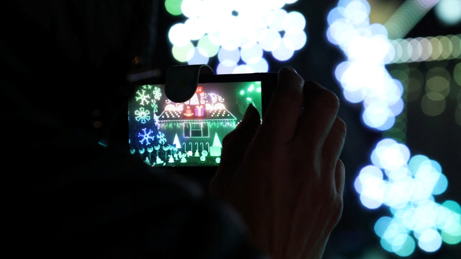 A person records video of a light show of a home decorated for Christmas.