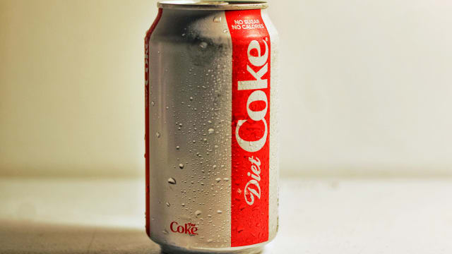 A sweating can of Diet Coke on a white surface against a white background. 