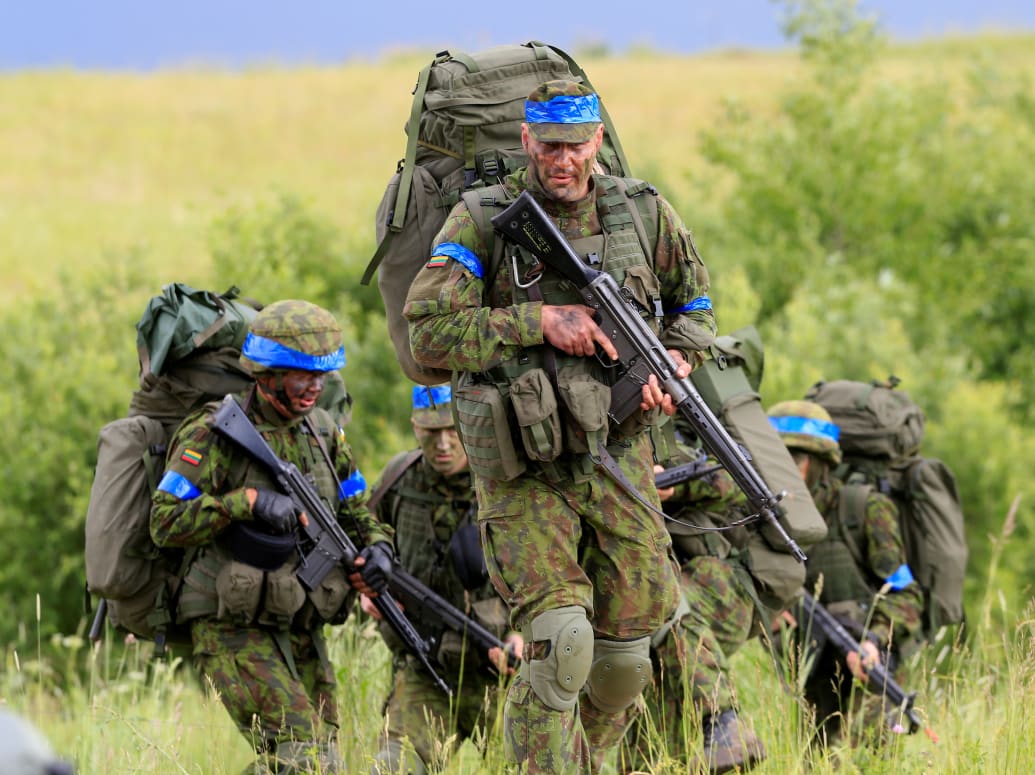 Lithuanian soldiers, wearing face paint and blue tape on their helmets, complete an exercise near the Suwałki Gap.