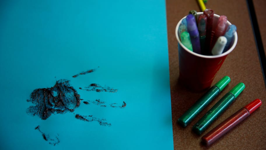 A handprint in glitter glue next to a cup of glitter pens 