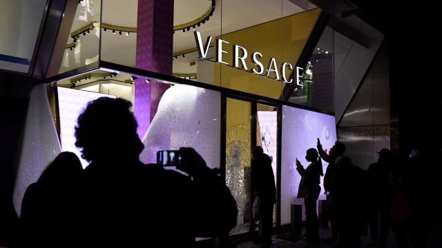 People take pictures with their mobilephones of the broken window of the Versace store after clashes following a demonstration in Barcelona on February 20, 2021.
